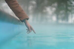 Hand of woman checking temperature of water in open swimming pool in winter. Thermal spa outdoor.